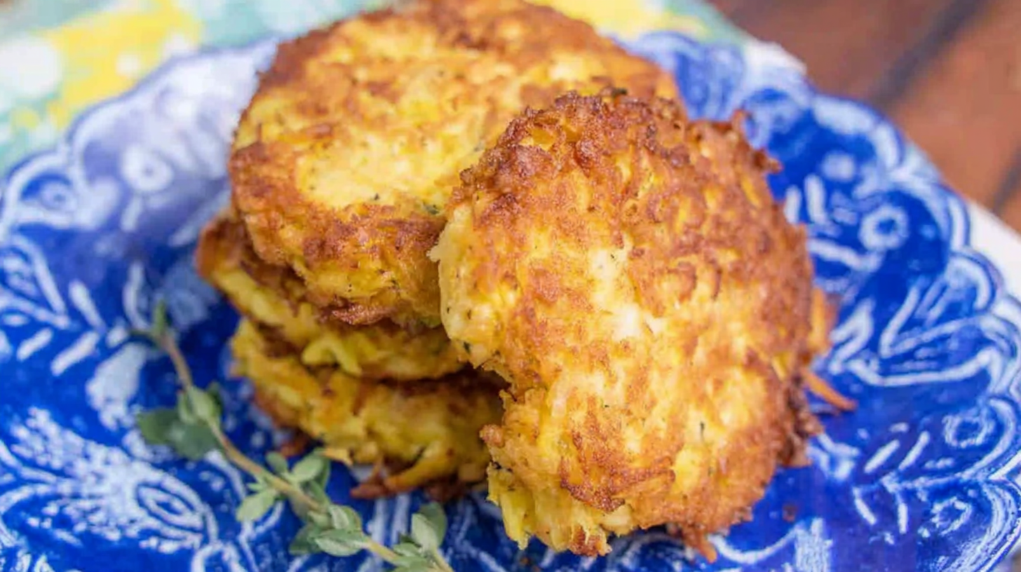 Golden brown squash patties stacked on a plate with herbs