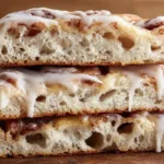 Cinnamon Roll Focaccia topped with icing on a wooden surface.