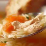 Bowl of delicious Lemon Chicken Orzo Soup garnished with herbs and lemon slices.