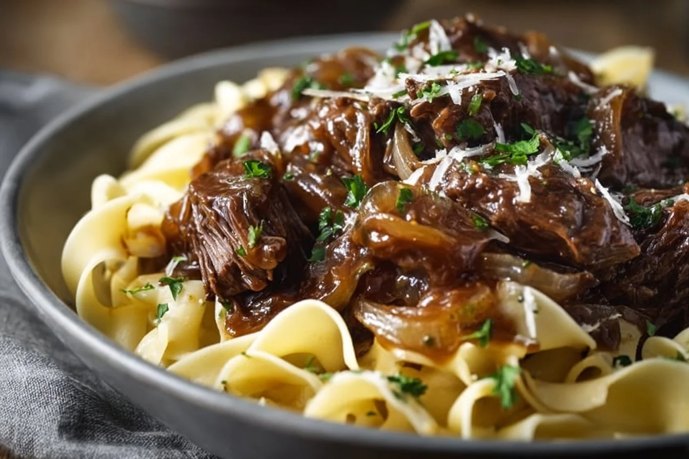 Delicious plate of French onion beef and noodles garnished with fresh herbs.